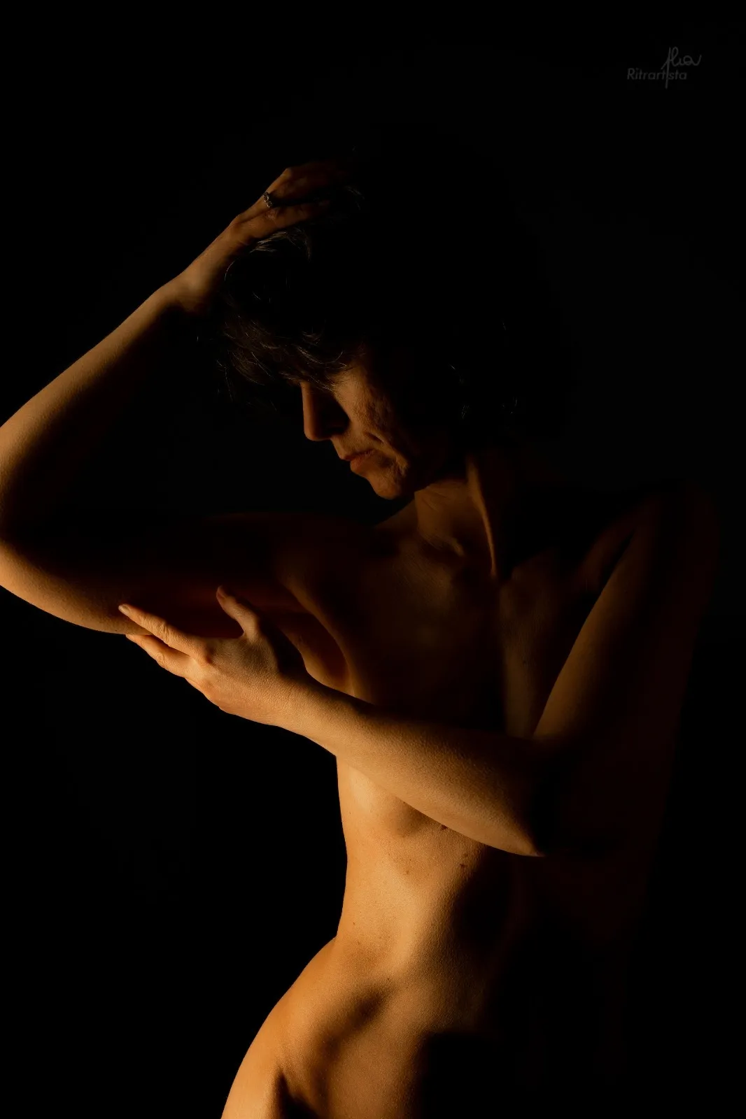 Nudo in luce calda su fondo nero, braccia incrociate