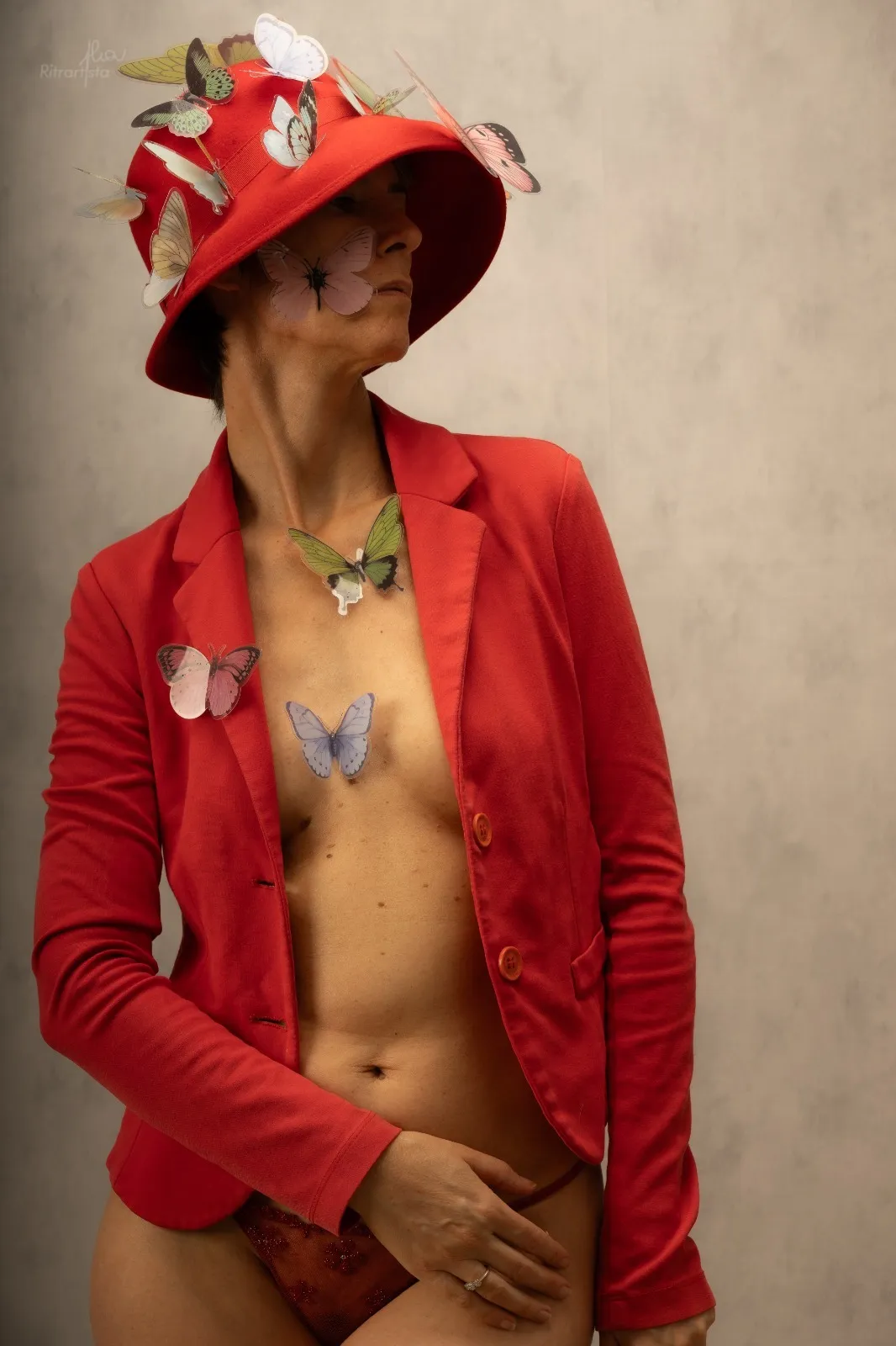 Donna con giacca rossa e cappello di farfalle, sguardo di lato