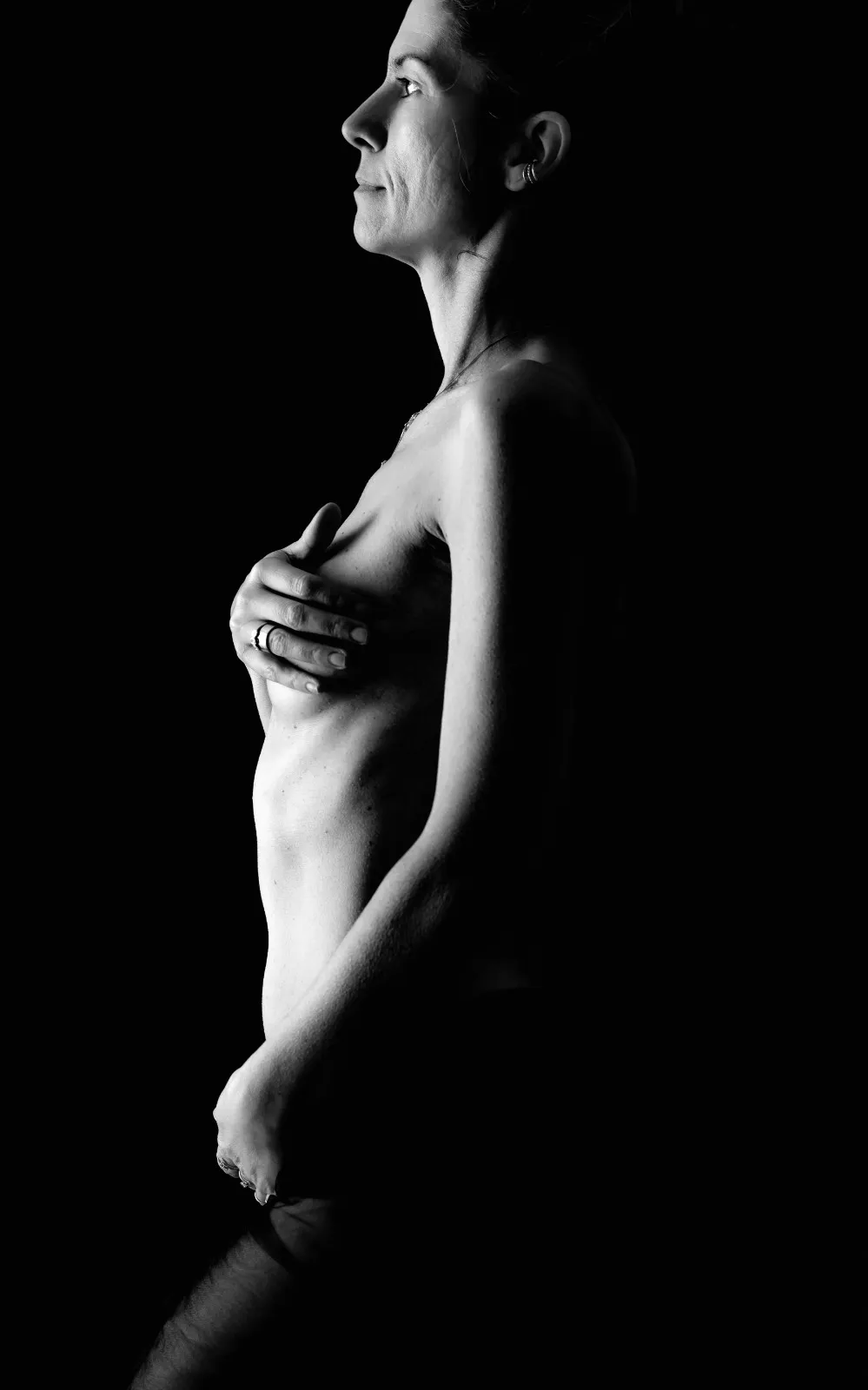 Donna di profilo in bianco e nero su fondo nero, mano sul seno