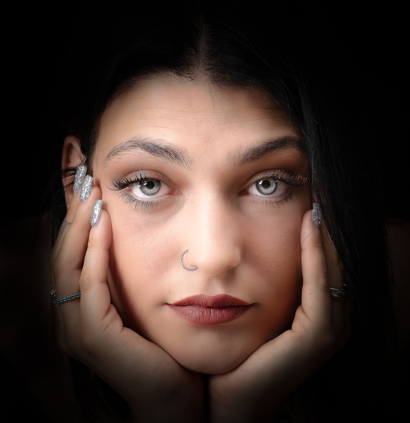 Ritratto d'autore di giovane donna con le mani sul viso, in luce calda su fondo nero
